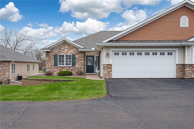 view of front of house with driveway, roof with shingles, a front lawn, an attached garage, and stone siding