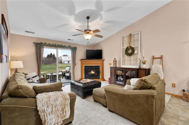 living room with ceiling fan, vaulted ceiling, a glass covered fireplace, and visible vents