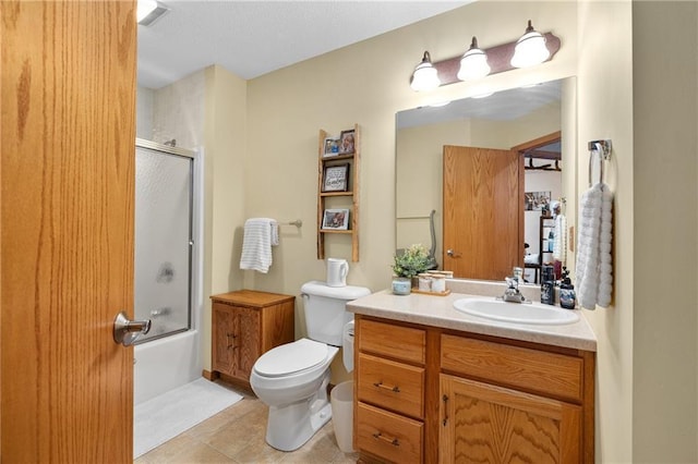 bathroom featuring toilet, combined bath / shower with glass door, tile patterned flooring, and vanity