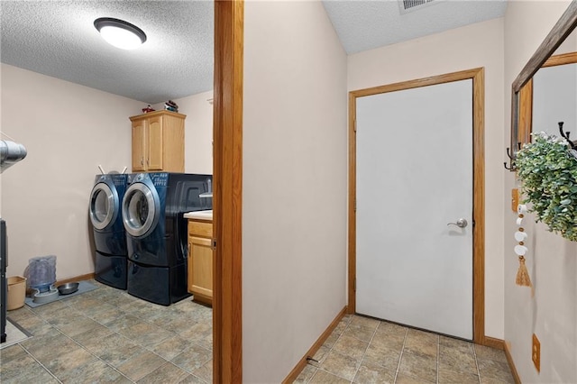 laundry room featuring stone finish flooring, a textured ceiling, cabinet space, baseboards, and washer and clothes dryer