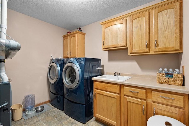 clothes washing area featuring a sink, cabinet space, a textured ceiling, and washing machine and clothes dryer