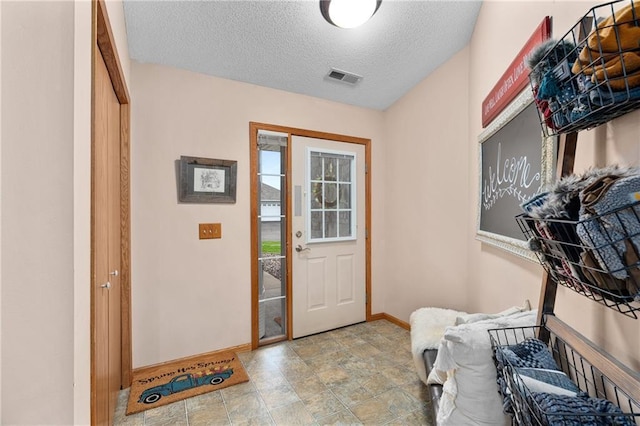 entryway with baseboards, a textured ceiling, visible vents, and stone finish floor
