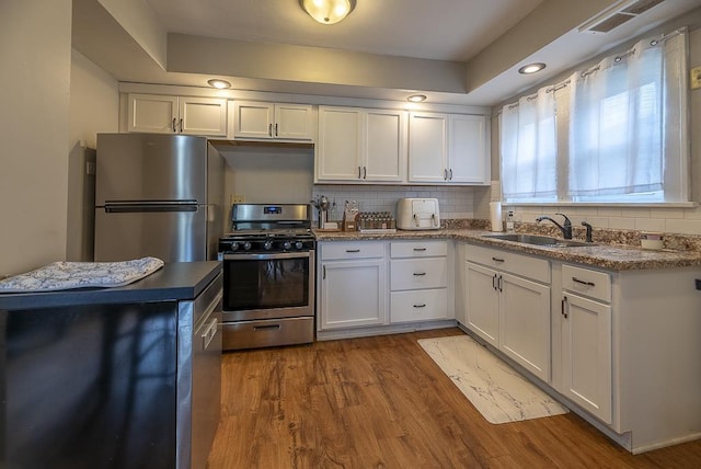 kitchen featuring a sink, stainless steel appliances, white cabinetry, and wood finished floors