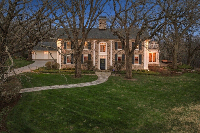 view of front of house featuring driveway, a chimney, a garage, a front lawn, and stone siding