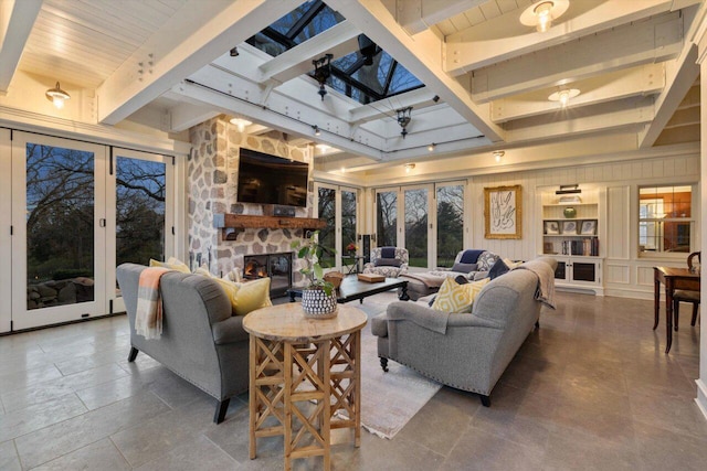 living area with a skylight, beamed ceiling, and a stone fireplace