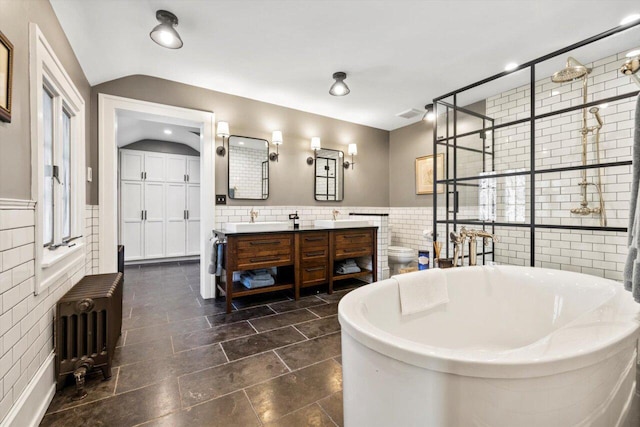 bathroom with double vanity, radiator, lofted ceiling, tile walls, and a soaking tub