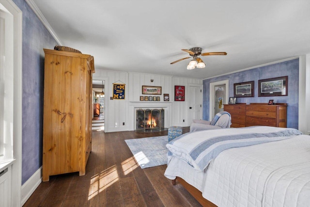 bedroom with ceiling fan, ornamental molding, a lit fireplace, and dark wood-style floors