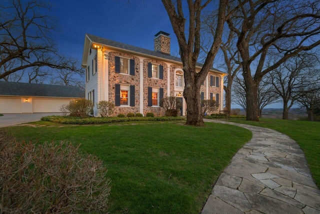 view of front of property with a garage, stone siding, a front yard, a chimney, and concrete driveway
