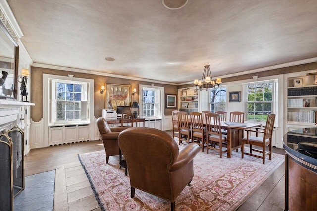 dining space with crown molding, a notable chandelier, a decorative wall, a fireplace with flush hearth, and hardwood / wood-style flooring