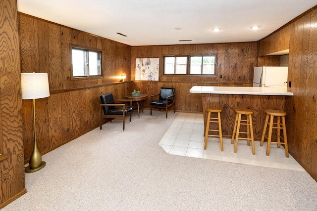 kitchen featuring freestanding refrigerator, wooden walls, and light carpet
