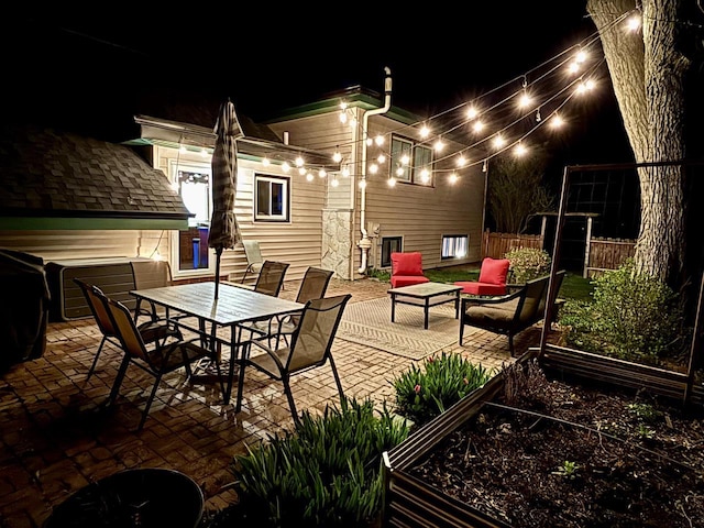 patio at night with fence, a garden, and outdoor dining space