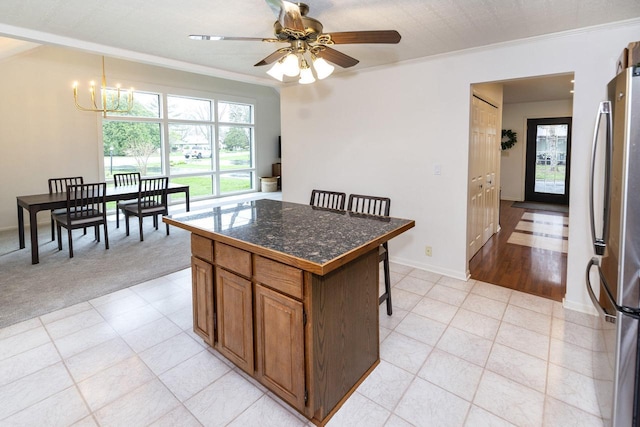 kitchen with brown cabinetry, freestanding refrigerator, crown molding, dark countertops, and a center island