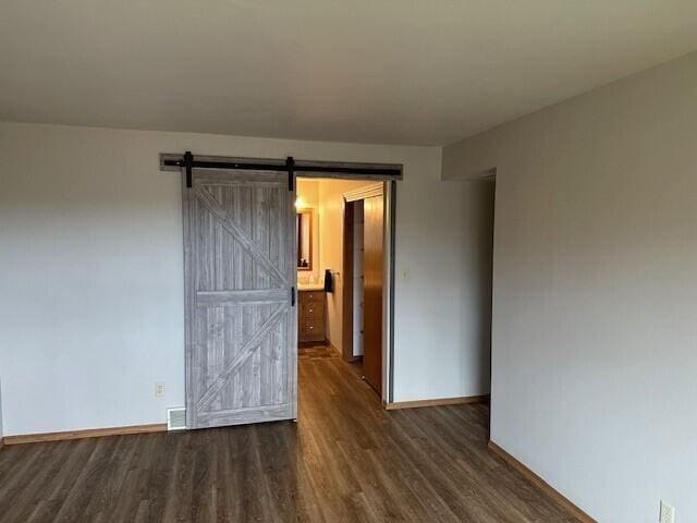 empty room featuring baseboards, a barn door, dark wood finished floors, and visible vents