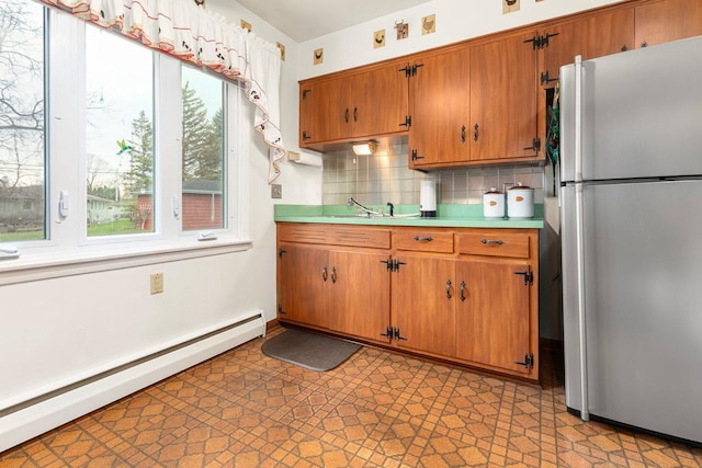 901 E Grant St, Appleton, WI 54911 - kitchen with tasteful backsplash, baseboard heating, brown cabinets, light countertops, and freestanding refrigerator