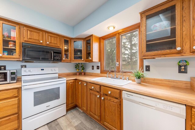 kitchen featuring a sink, brown cabinets, white appliances, and glass insert cabinets