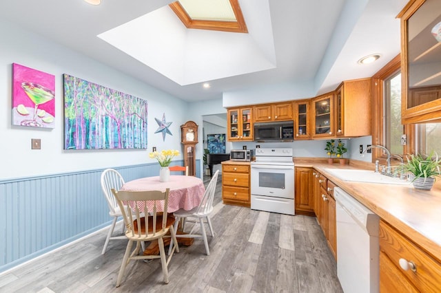 kitchen with brown cabinetry, white appliances, light countertops, a sink, and light wood finished floors