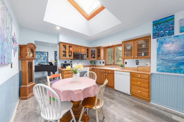 kitchen with a sink, brown cabinets, light wood-type flooring, and white appliances