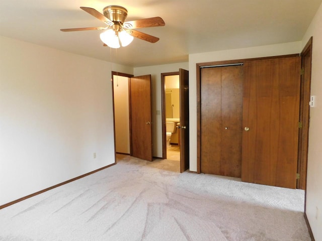 unfurnished bedroom featuring a closet, baseboards, ceiling fan, light colored carpet, and ensuite bath