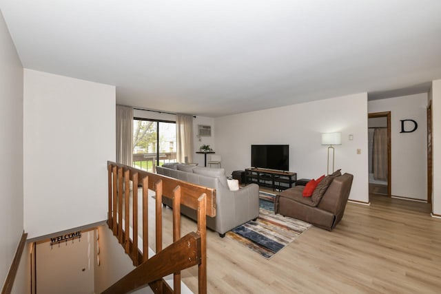 living area featuring baseboards, light wood-type flooring, and a wall mounted air conditioner