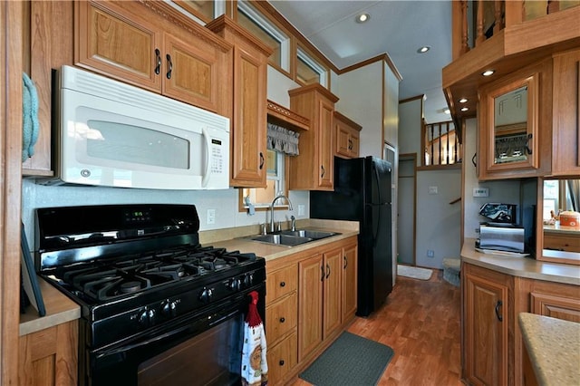 kitchen featuring brown cabinetry, light countertops, a sink, light wood finished floors, and black appliances