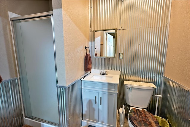 bathroom with wainscoting, a textured wall, a stall shower, and toilet