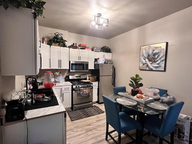 kitchen featuring light wood-style floors, light countertops, white cabinetry, a sink, and appliances with stainless steel finishes