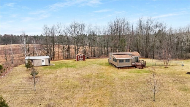 view of yard featuring a wooded view, an outdoor structure, a deck, and a storage unit