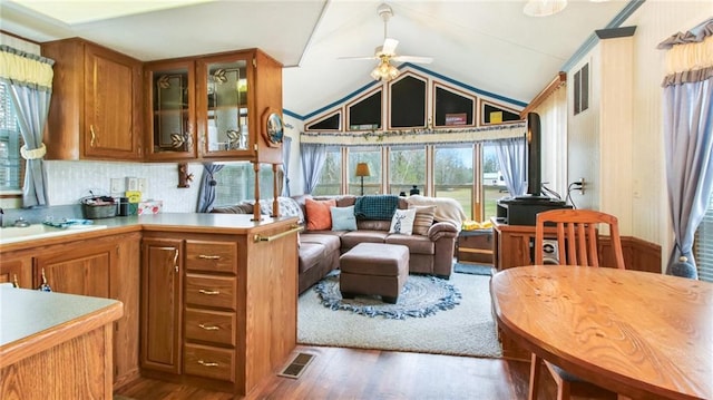 interior space with glass insert cabinets, wood finished floors, a ceiling fan, brown cabinets, and visible vents