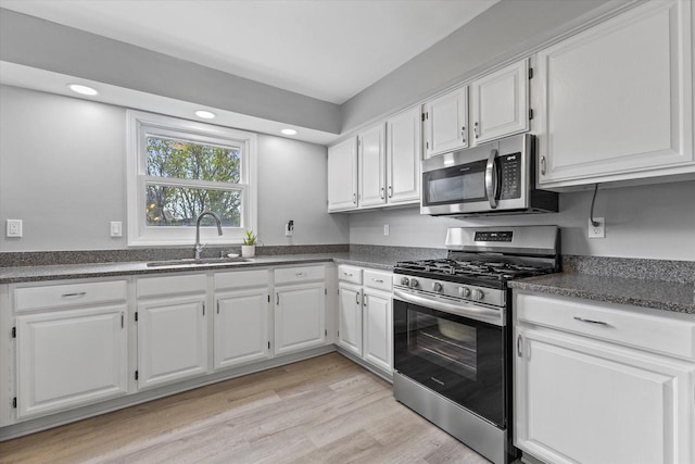 kitchen featuring dark countertops, light wood-style floors, white cabinetry, a sink, and stainless steel appliances