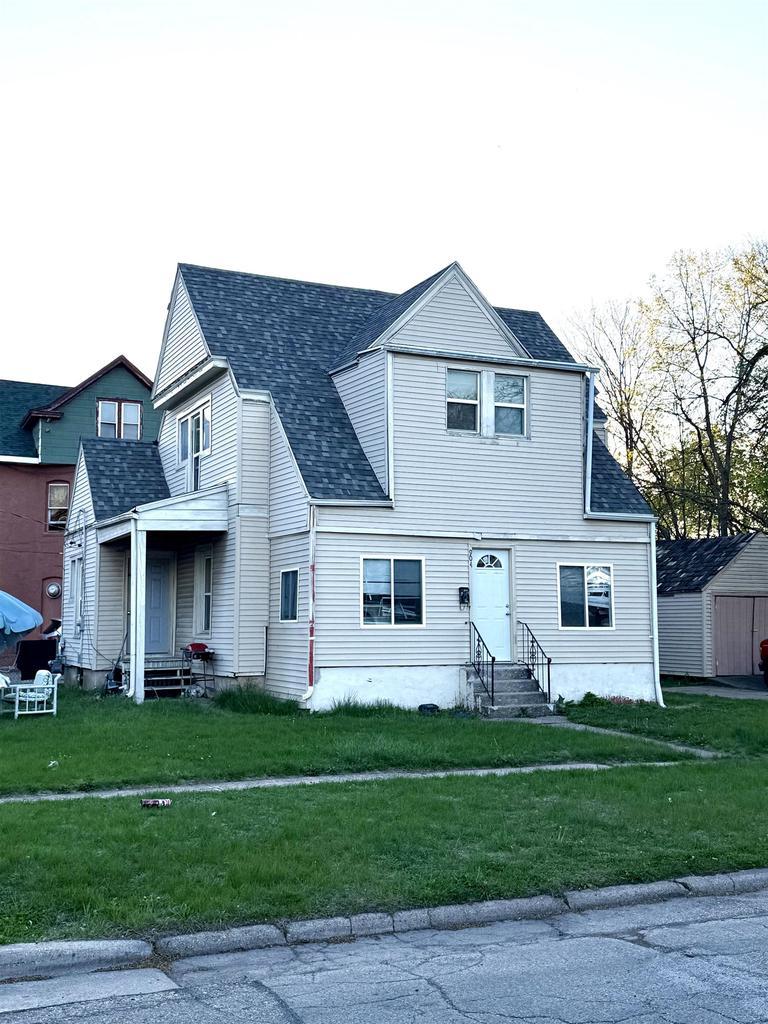view of front facade featuring entry steps, roof with shingles, and a front yard
