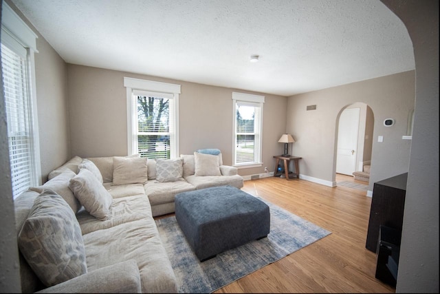 living room featuring baseboards, arched walkways, and light wood finished floors