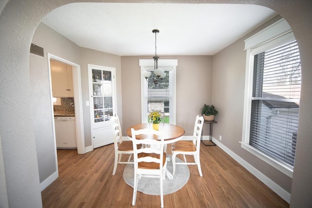 dining area with baseboards, arched walkways, wood finished floors, and an inviting chandelier