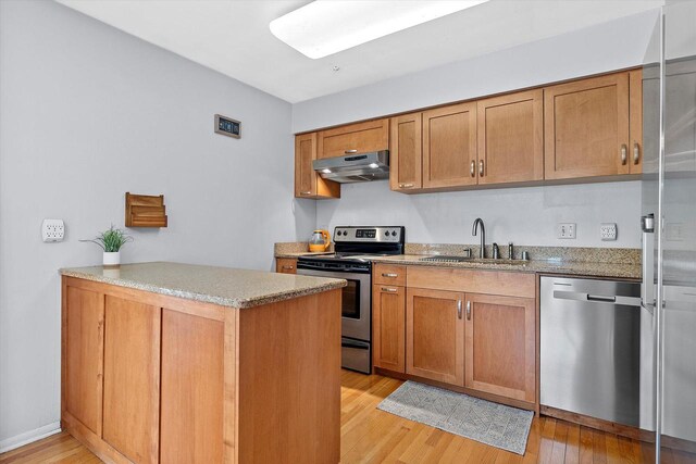 kitchen featuring under cabinet range hood, brown cabinets, a sink, light wood-style flooring, and stainless steel appliances