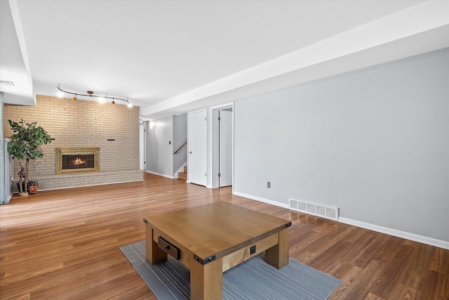 living room with visible vents, a brick fireplace, rail lighting, wood finished floors, and stairway