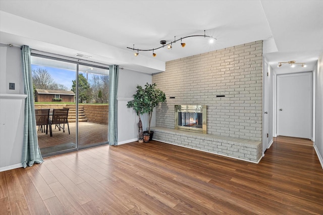 unfurnished living room with track lighting, a fireplace, brick wall, wood finished floors, and visible vents
