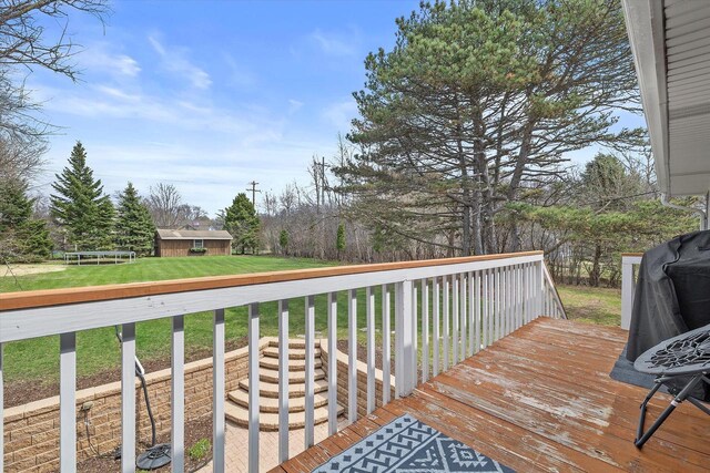 wooden deck with an outbuilding, a trampoline, and a yard