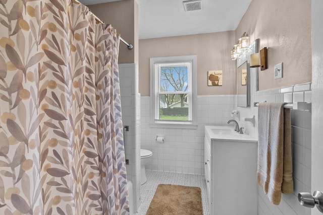 bathroom with visible vents, vanity, toilet, tile walls, and tile patterned floors