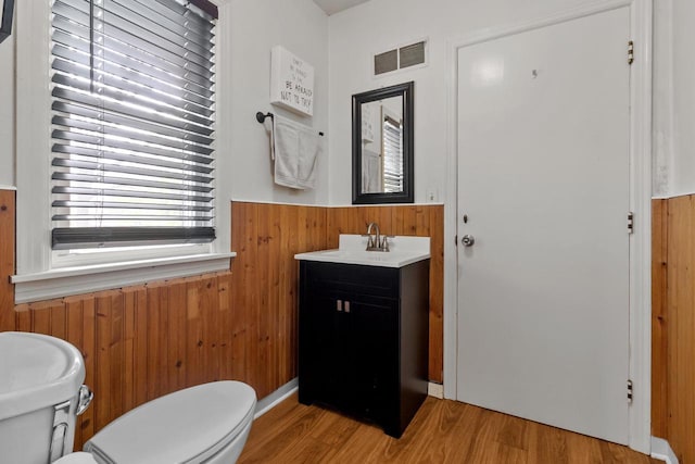 half bath featuring visible vents, wood walls, wood finished floors, toilet, and a wainscoted wall