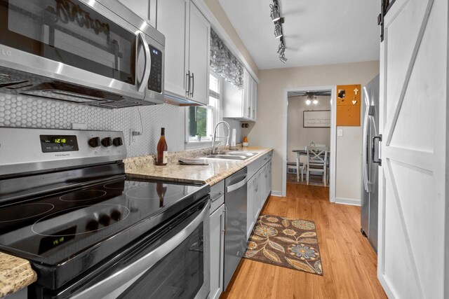 kitchen featuring decorative backsplash, light wood-type flooring, white cabinetry, a sink, and stainless steel appliances