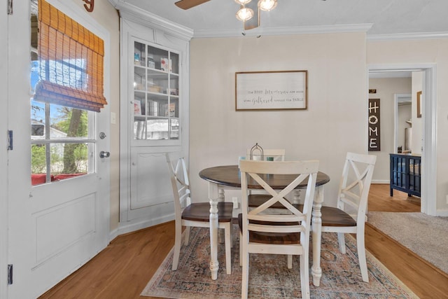 dining room with crown molding, baseboards, a ceiling fan, and wood finished floors