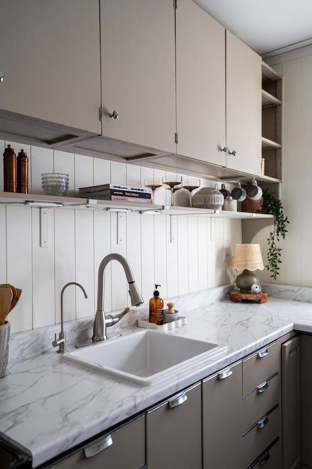 kitchen with gray cabinets, open shelves, light stone counters, and a sink