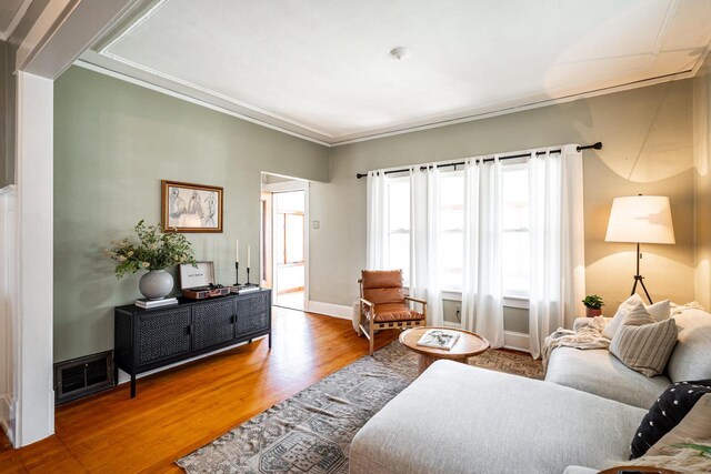 living room featuring crown molding, baseboards, wood finished floors, and visible vents