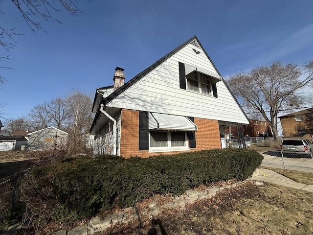 view of side of property with brick siding, fence, and a chimney