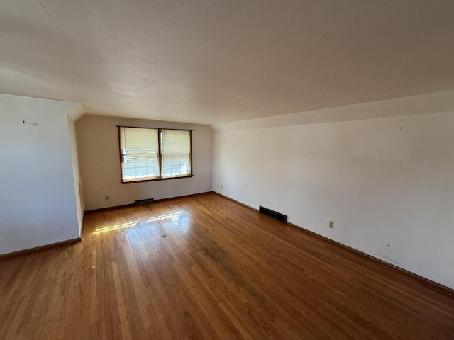 empty room featuring baseboards, wood finished floors, and visible vents