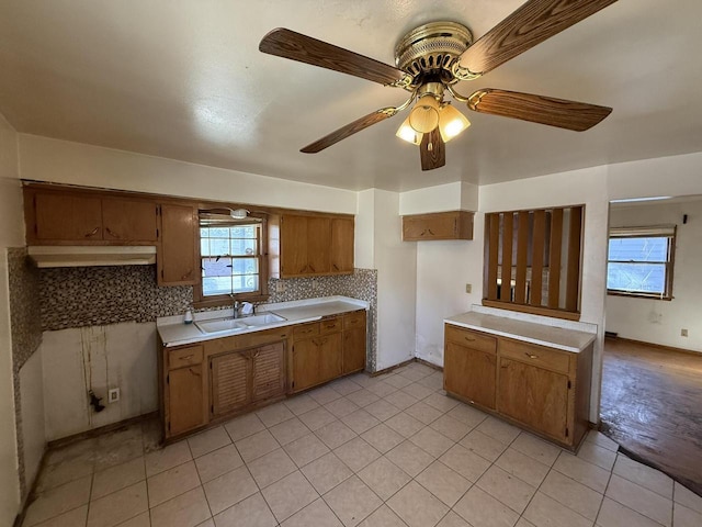 kitchen featuring a sink, backsplash, brown cabinets, and light countertops