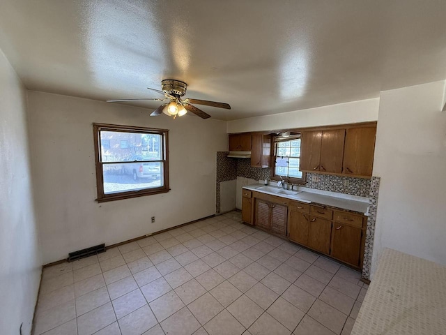 kitchen with ceiling fan, a sink, brown cabinetry, decorative backsplash, and visible vents