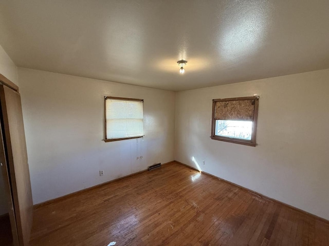 empty room featuring a healthy amount of sunlight, baseboards, hardwood / wood-style flooring, and visible vents