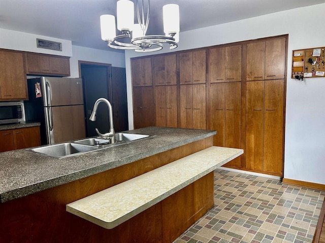 kitchen with dark countertops, appliances with stainless steel finishes, an inviting chandelier, a sink, and baseboards