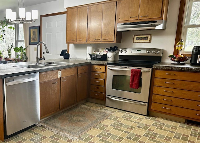 kitchen with a peninsula, under cabinet range hood, brown cabinets, a sink, and stainless steel appliances
