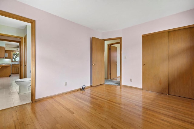 unfurnished bedroom with baseboards, ensuite bathroom, a closet, and light wood finished floors